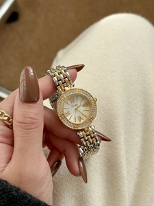 Close-up of a two-tone metal watch featuring a diamond-set bezel and a white roman dial