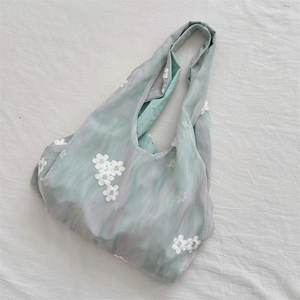 Close-up of light green canvas tote with white floral embroidery on soft fabric