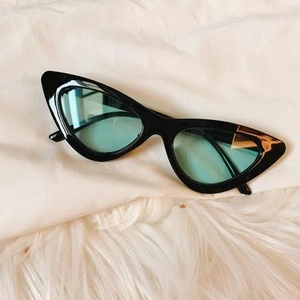 Retro black cat-eye sunglasses with light blue lenses on white fabric backdrop