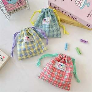 Three colorful checkered drawstring storage bags with woven labels on a white desk