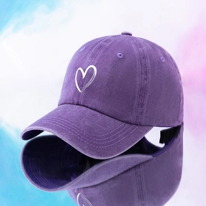 Washed dark purple baseball cap with white heart embroidery, mirrored view on blue background