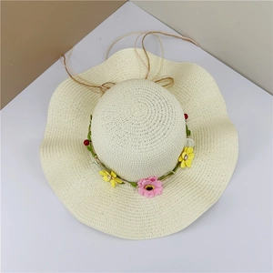 Close-up of cream straw sun hat with wavy brim and colorful floral daisy wreath decoration