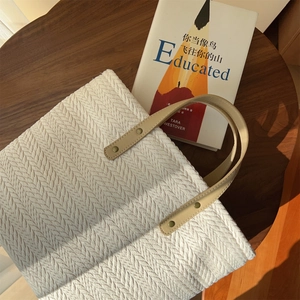 Detailed weave pattern of a beige canvas tote bag with leather handles on a wooden table