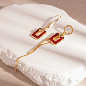 Detail of gold geometric earrings with red resin inlay and long chain tassels