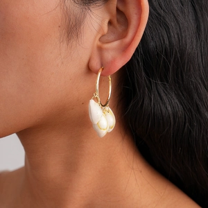 Close-up of bohemian gold hoop earrings with white natural cowrie shell pendants
