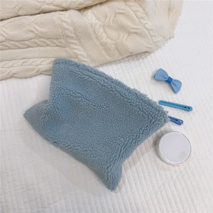 Close-up of soft blue sherpa fleece makeup bag on a cozy knitted texture background