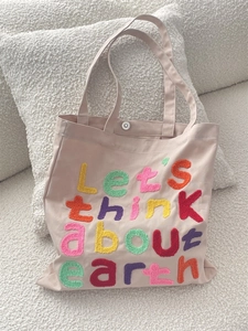 Detail of colorful chenille embroidery text on a pink canvas tote bag with metal button