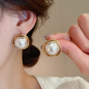 Detail of round faux pearl earrings with golden spiral metal base on model