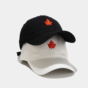 Black and beige baseball caps with maple leaf embroidery on a gray background