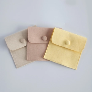 Detail of square velvet jewelry pouches with snap buttons in beige, pink, and yellow