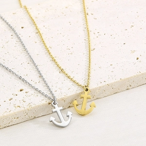 Close-up of anchor pendant necklaces in gold and silver finishes on stone background