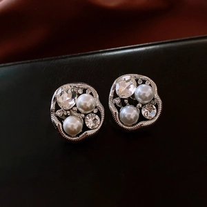 Macro shot of silver pearl earrings with crystals on black leather background
