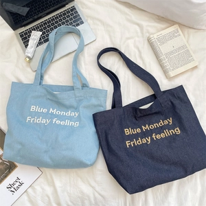 Dettaglio di borse tote in denim blu con ricami su un lenzuolo bianco
