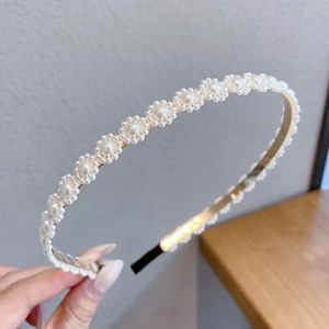 Close-up of golden metal headband with white pearl flower details held by hand