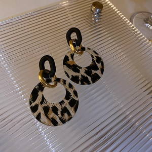 Detail of leopard print earrings with matte black links and golden metal rings on glass
