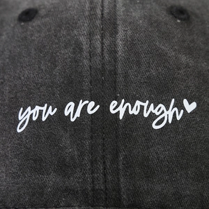 Close-up of you are enough slogan and heart embroidery on charcoal washed cotton cap