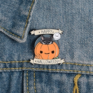 Macro view of Happy Halloween pumpkin and black cat metal pin on blue denim fabric