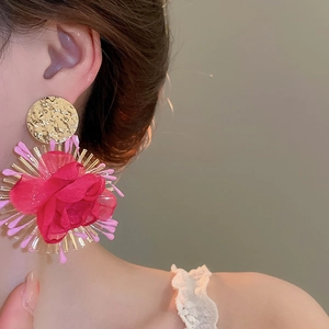 Close-up of gold textured metal earrings with a handmade red silk rose and pink fringe detail