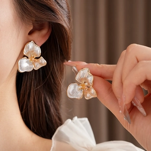 Close-up of a model wearing pearlescent white flower earrings with gold metal finish