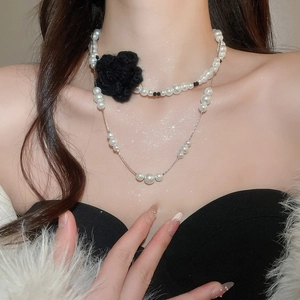 Detail of double-layered pearl necklace with black crochet flower on a female model
