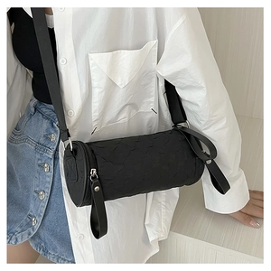 Detail of black cylindrical crossbody bag featuring textured fabric and wide strap