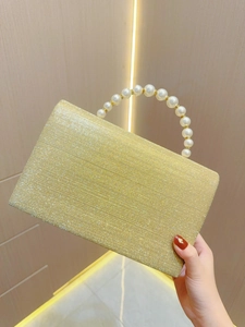 Close-up of champagne gold glitter evening clutch bag with elegant faux pearl handle