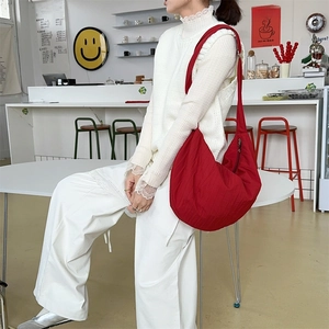 Detail view of large red crescent bag in pleated nylon fabric worn by model in a cafe