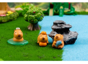 Detailed macro view of three miniature resin Capybara figurines in a lush mossy landscape