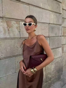Elegant brown satin slip dress styled with gold accessories and a burgundy woven clutch