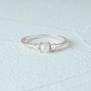 Macro shot of silver ring with white pearl and clear gemstones in a claw setting
