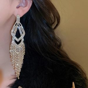 Macro shot of elegant long gold tassel earrings with shimmering crystals on a model
