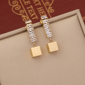 Detail of gold dangle earrings featuring zircon studs and a square floral pattern pendant