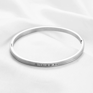 Detailed view of a silver stainless steel bangle with 7 inlaid cubic zirconia on white silk