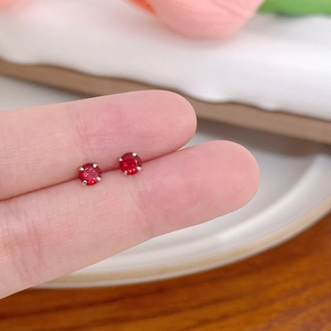 Macro shot of minimalist red zircon stud earrings held between fingers for size reference