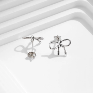 Minimalist S925 sterling silver bow knot stud earrings on white geometric stairs
