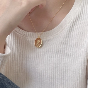 Close-up of golden oval rose flower embossed pendant necklace on white knit fabric