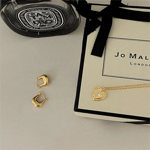 Close-up of golden heart pendant necklace and wing earrings on a cream surface