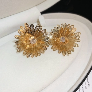 Close-up of golden geometric flower earrings with crystal center in a jewelry box