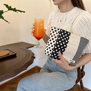 Polka dot fabric makeup bag held by a model in a cozy vintage cafe setting