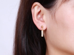 Close-up of gold cylindrical drop earrings with pavé set white zircon crystals on model