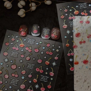 Detailed view of cherry nail art stickers with glitter effects on dark manicured nails