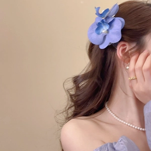Detail view of purple floral orchid hair clip with pearl embellishment on wavy hair