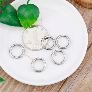 Five polished stainless steel open jump rings on white ceramic plate with a coin size reference