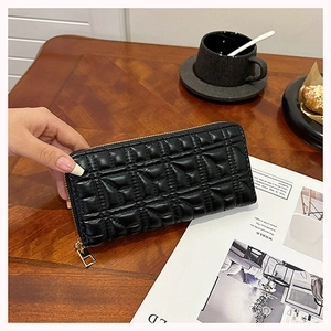Long black quilted clutch wallet with gold zipper on a wooden table with a coffee cup