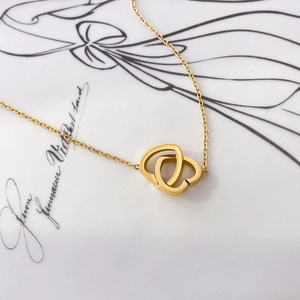 Macro shot of interlocking hearts pendant on gold chain necklace over aesthetic card
