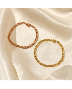 Detailed shot of gold and rose gold Figaro chain bracelets on elegant satin fabric
