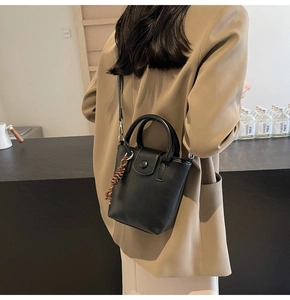 Rear view of a model carrying a black leather-style bucket bag with woven strap detail
