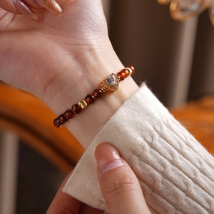 Detail of garnet beaded bracelet with gold heart charm worn on a model's wrist