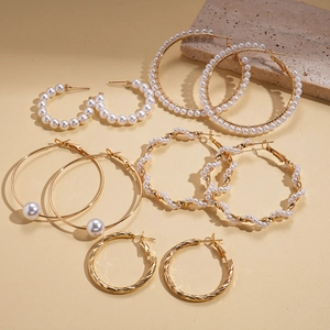 Close-up of 10-piece gold hoop earring set with white pearls on a textured stone surface