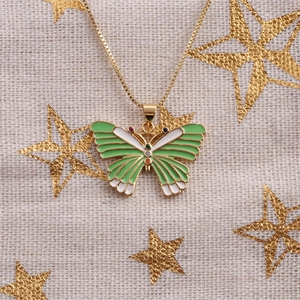 Close-up of gold butterfly necklace with green and white enamel on a starry background